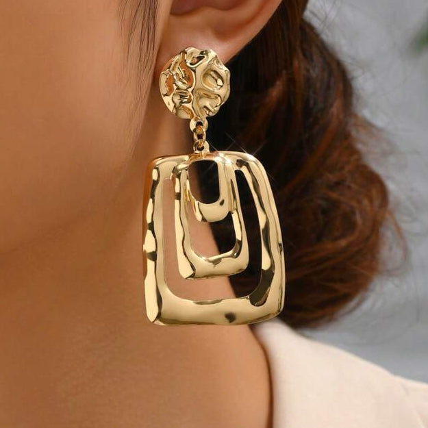 Gold earrings worn by a person with a neutral background