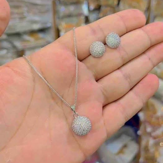 A hand holding a silver pendant necklace and a pair of silver earrings with clear crystals.