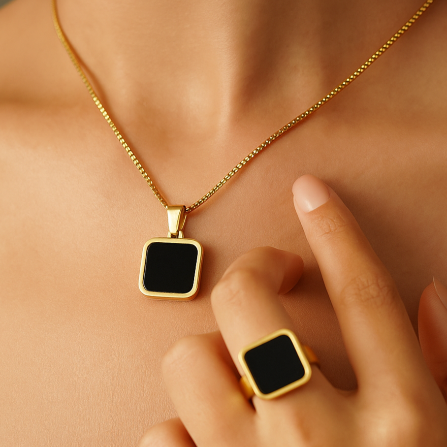 Gold necklace and ring with black square pendants on a person's neck and hand.