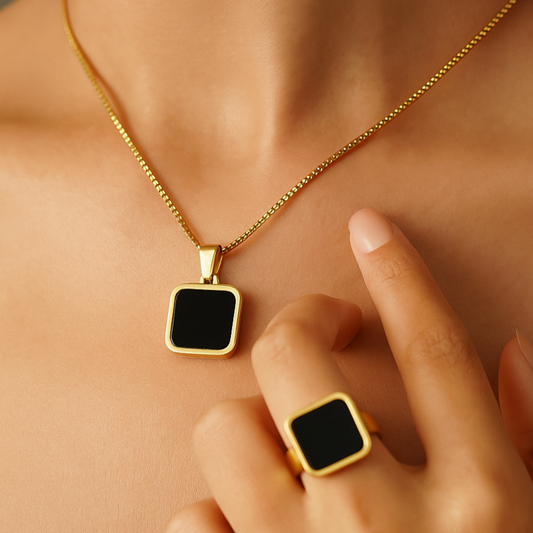 Gold necklace and ring with black square pendants on a person's neck and hand.