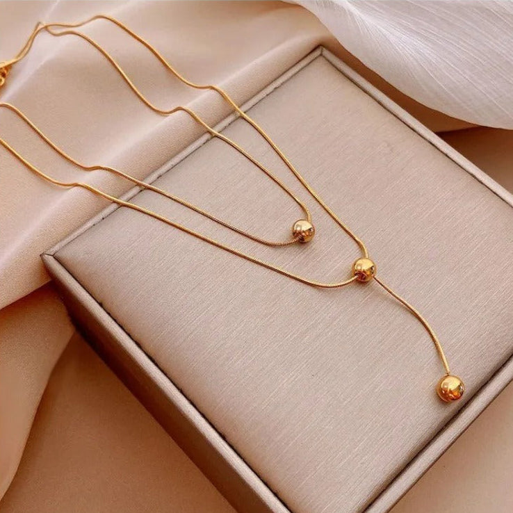 Gold necklace displayed on a pink stand and worn by a person.