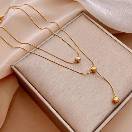 Gold necklace displayed on a pink stand and worn by a person.