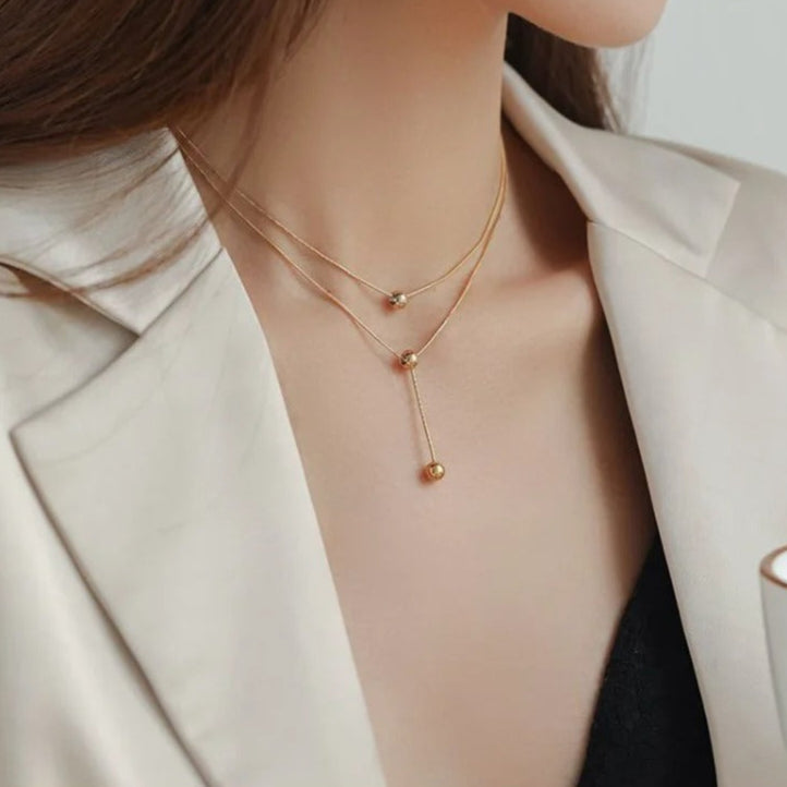 Gold necklace displayed on a pink stand and worn by a person.