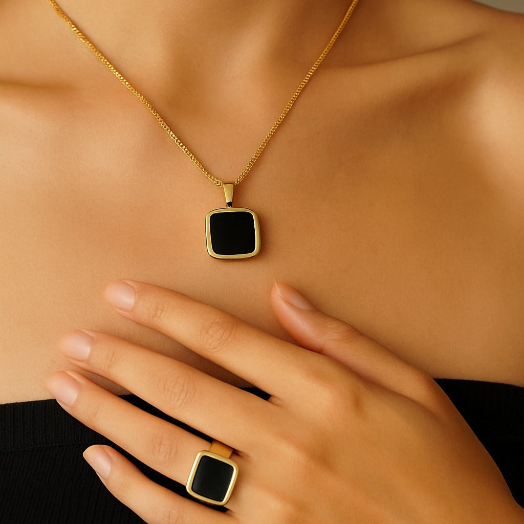 Gold necklace and ring with a black square pendant on a neutral background