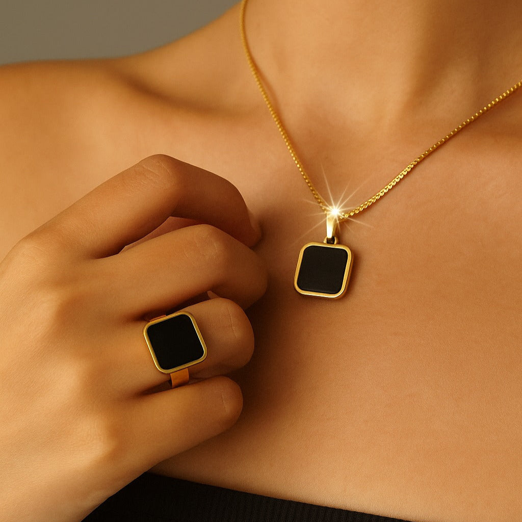 Person wearing a gold necklace with a square pendant, hand touching the chest.